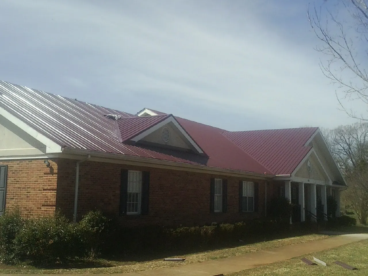 Red metal roof with gabled entries on a long brick building, from a Hail Damage Roof Repair job in Enoree