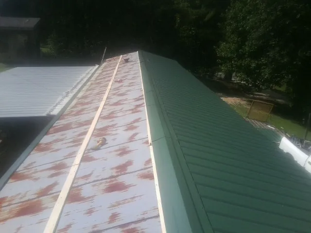 Old rusted panels beside newly installed green metal roofing — Wind Damage Roof Repair by Roofing Brothers in Enoree