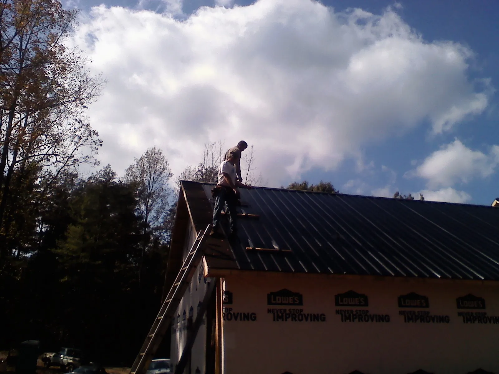 Roofer fastening dark metal panels high against a cloudy sky, from a Roof Inspection job in Enoree